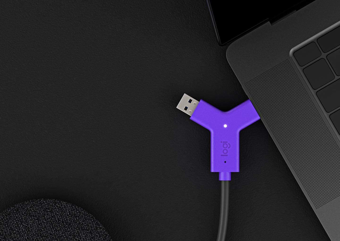 Adattatore USB-C Logitech viola collegato a un laptop, su una scrivania nera.