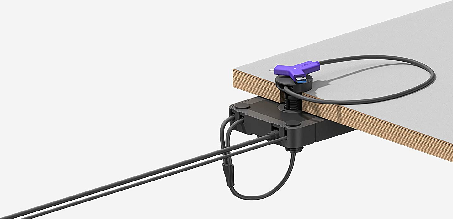Adattatore multiporta nero e viola fissato a una scrivania in legno chiaro. I cavi si estendono verso sinistra.