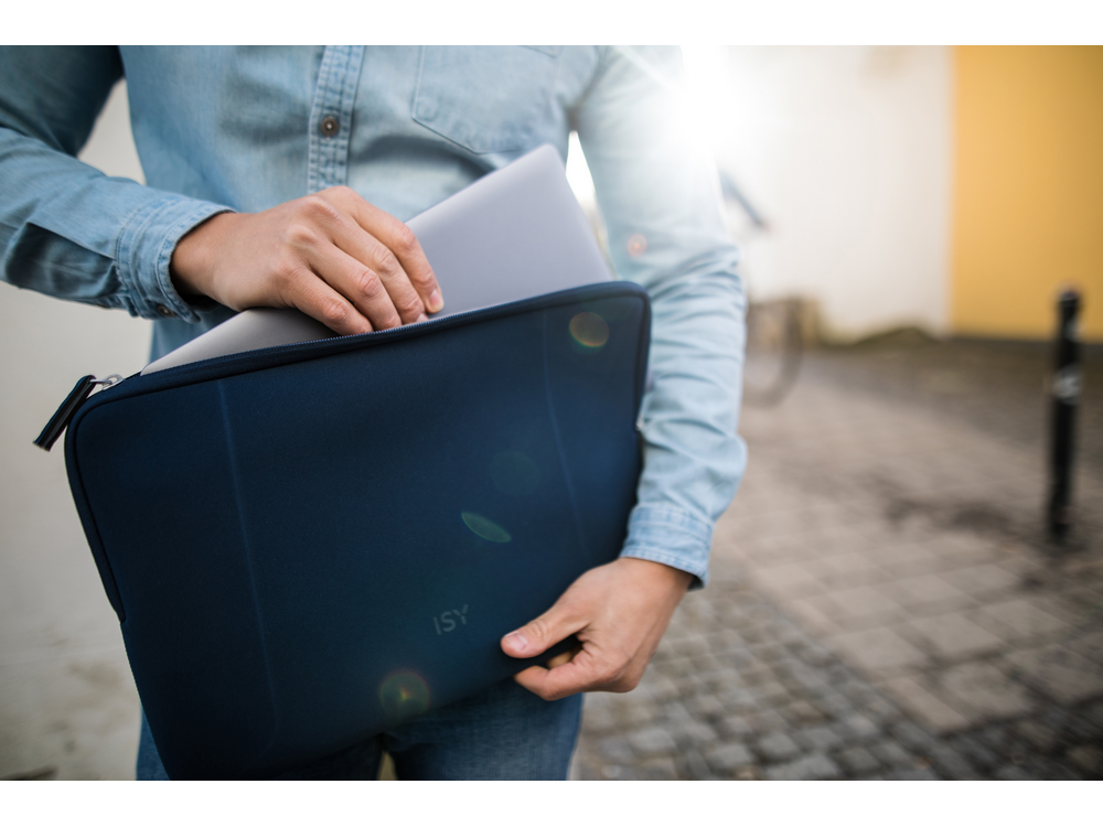 Una persona sostiene una computadora portátil en una funda azul, al aire libre con luz solar.