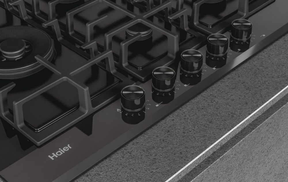 Estufa de gas Haier negra con quemadores y perillas de control, sobre encimera.