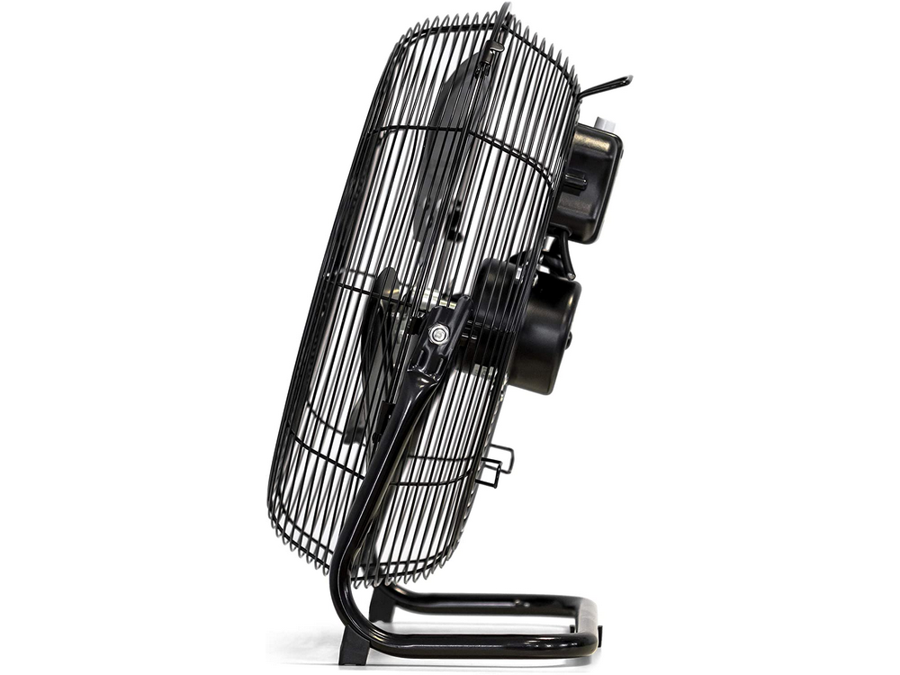 Ventilador de metal negro sobre un soporte. Tiene una jaula alrededor de las aspas.
