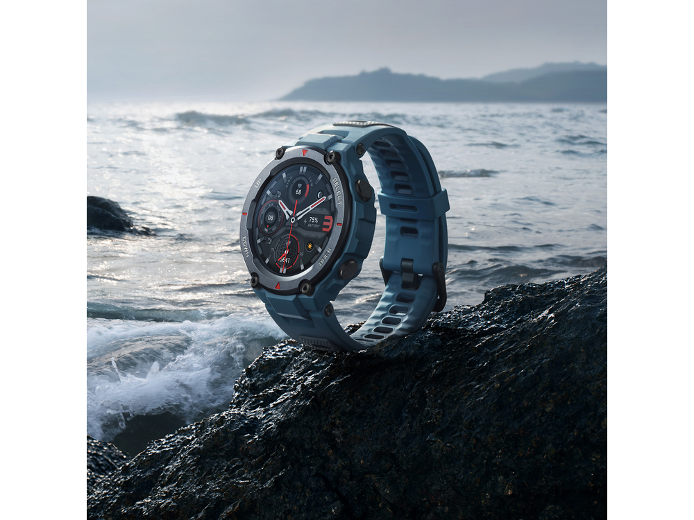 Un reloj inteligente azul sobre una roca con olas al fondo.