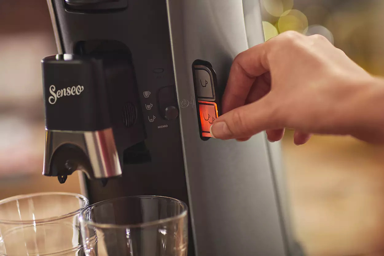 Une main appuyant sur un bouton d'une cafetière, avec deux verres au premier plan.