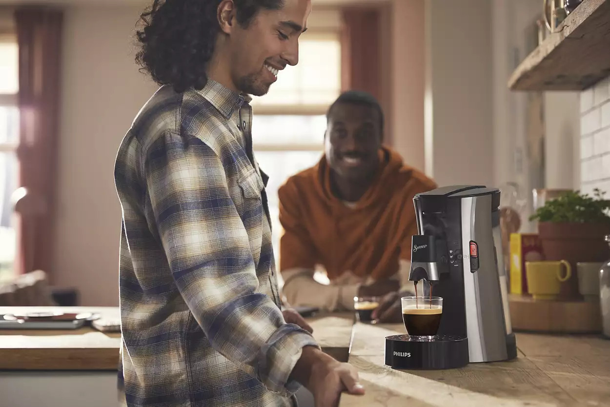Un homme prépare du café avec une cafetière. Un autre homme est à l'arrière-plan.