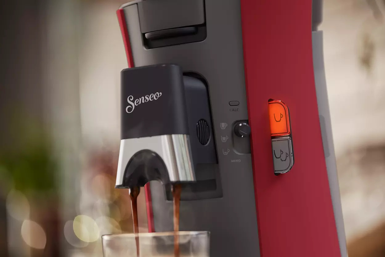 A red and black coffee machine with coffee pouring into a glass.