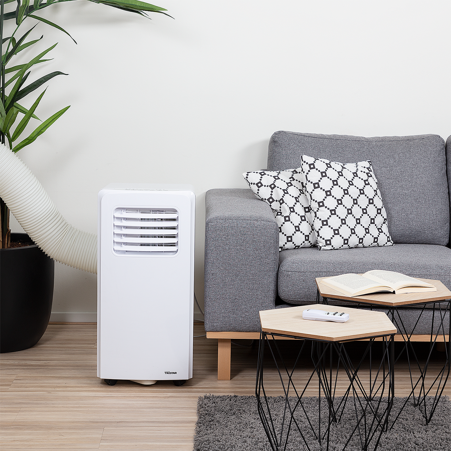 White portable air conditioner next to a gray couch with pillows and tables.