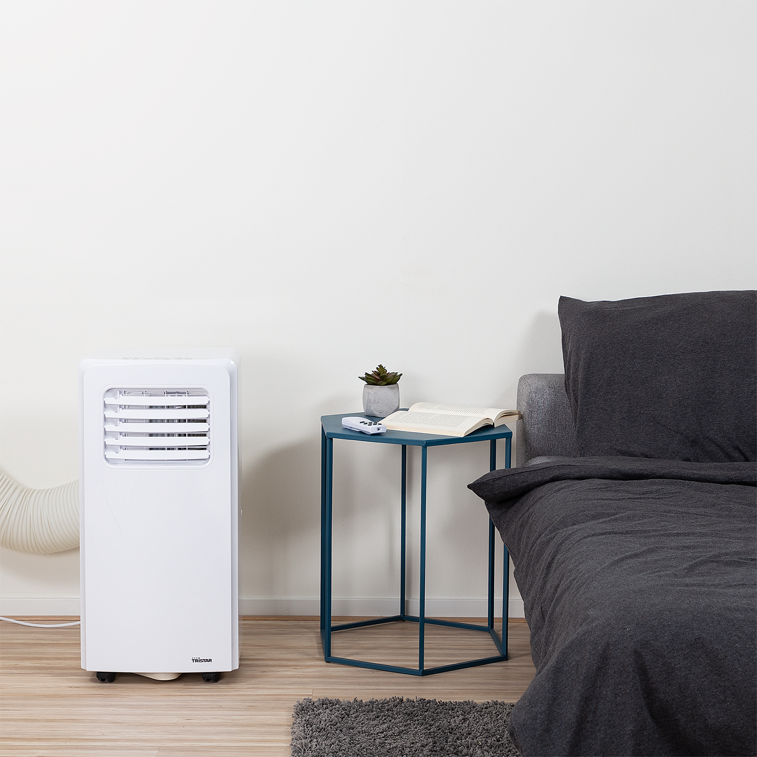 White air conditioner, small table with book and plant, and a bed.