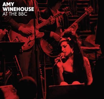 Amy Winehouse zingt op het podium met een band. De afbeelding is in roodtinten.