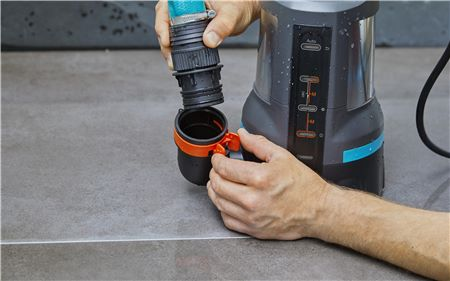Eine Person verbindet einen Schlauch mit einer Tauchpumpe. Die Pumpe ist schwarz und orange.