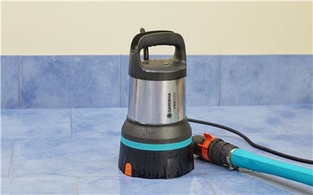 Eine schwarz-silberne Wasserpumpe steht auf einem blau gefliesten Boden. Ein blauer Schlauch ist angeschlossen.