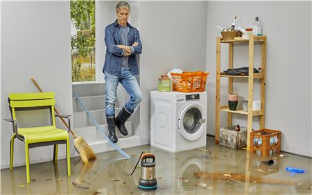 Mann im überfluteten Keller, steht an der Treppe, blickt auf Wasser und Trümmer.