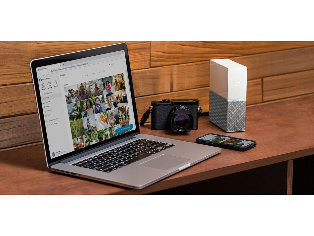 Portátil, cámara, teléfono y disco duro externo sobre una mesa de madera.