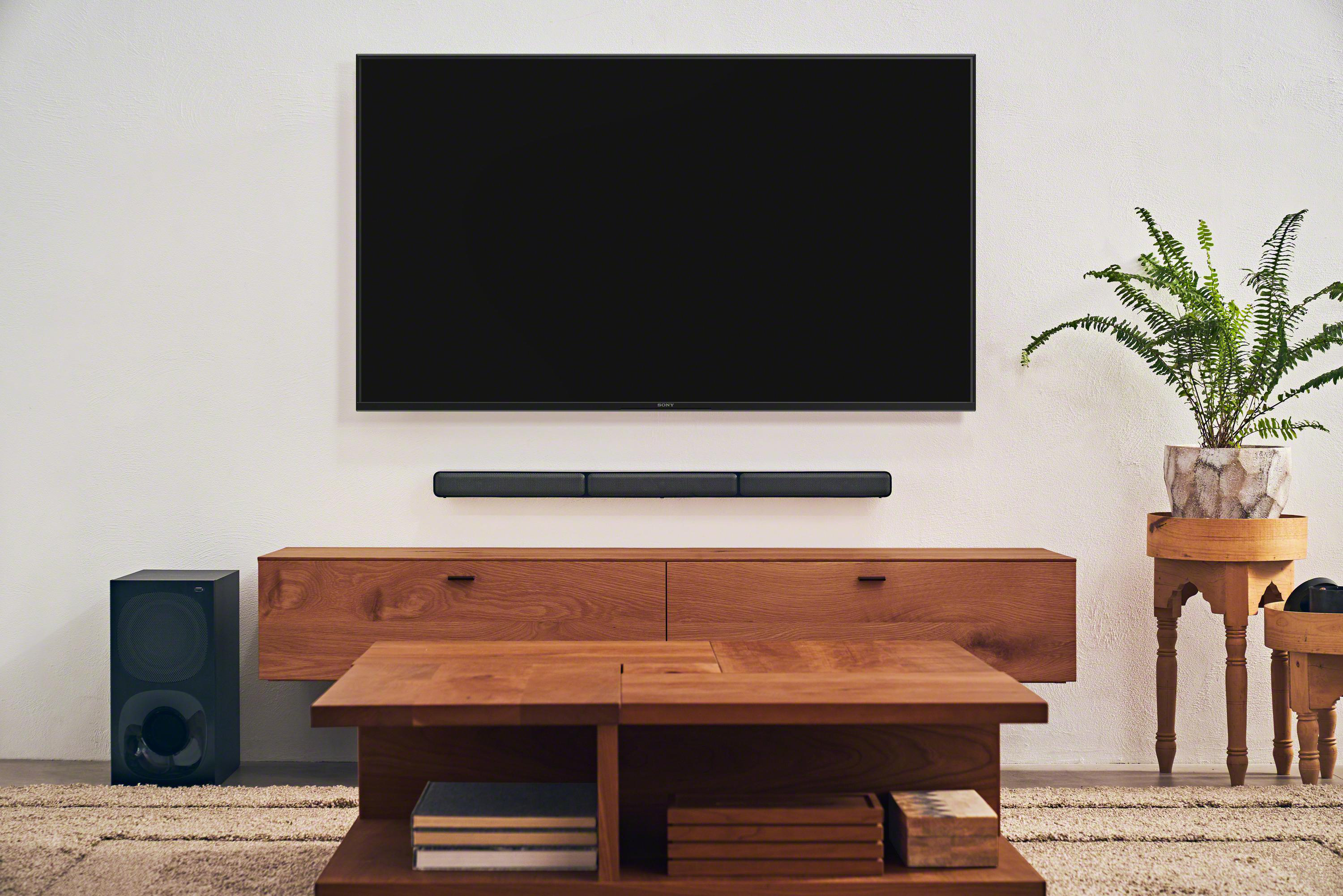 Wohnzimmer mit Fernseher, Soundbar, Subwoofer und Tisch.