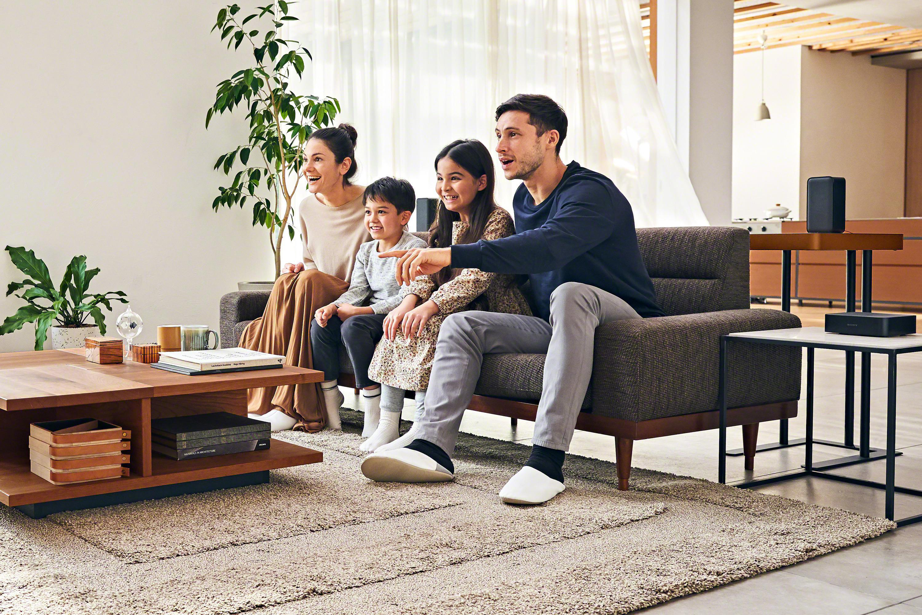 Familie schaut fern. Ein Sofa, ein Couchtisch und Lautsprecher befinden sich in einem Wohnzimmer.