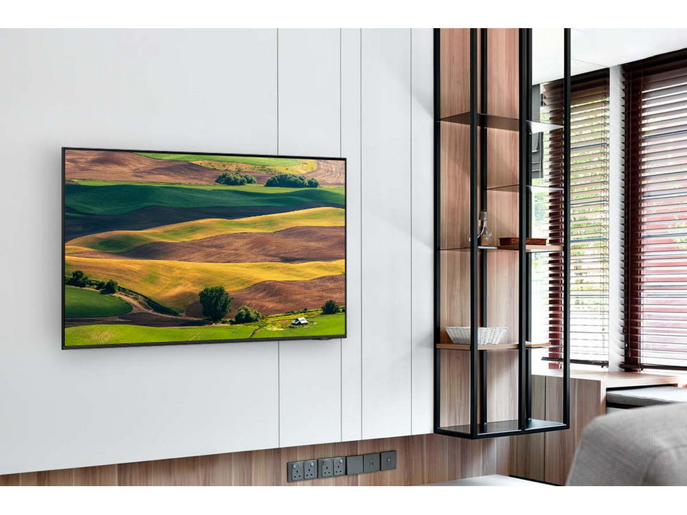 TV montado en pared blanca, mostrando paisaje, con estante de madera.