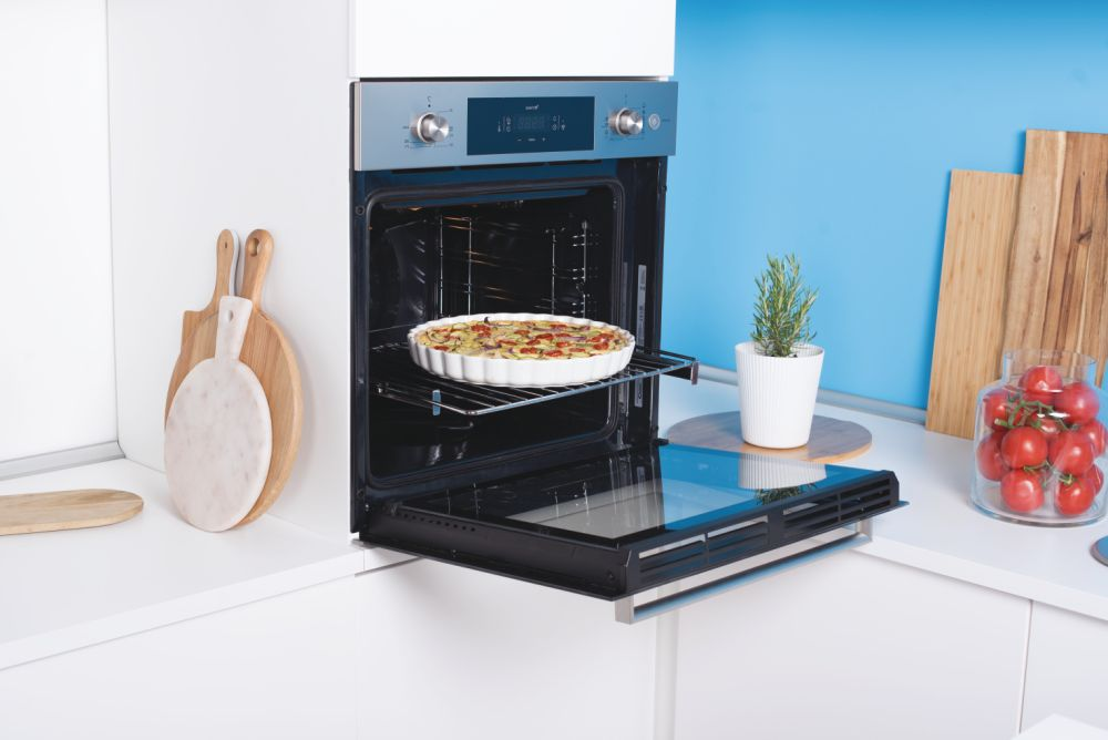 Horno abierto con un plato horneado dentro, ubicado en una cocina blanca moderna.