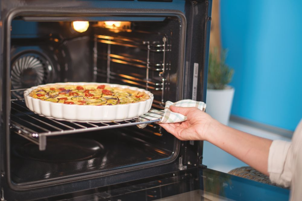 Horno con tarta. Mano con guante sacando la tarta.