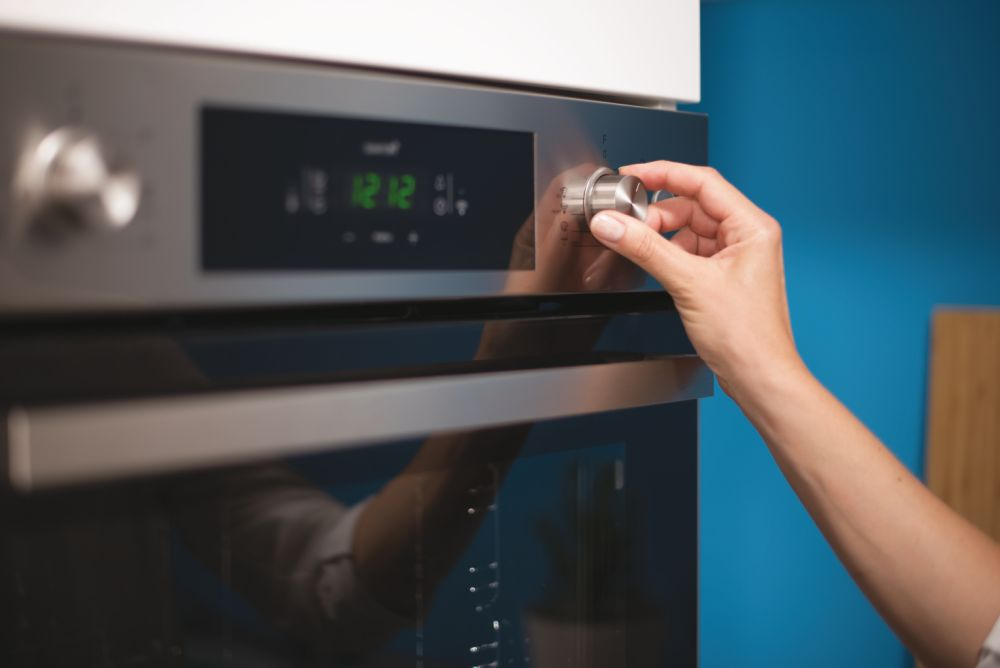 Una mano girando un dial en un horno oscuro, posiblemente ajustando la temperatura o un temporizador.