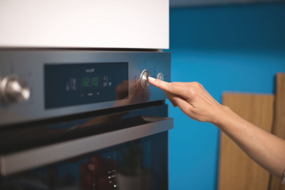 Mano presionando un botón en un horno con pantalla digital 12:10.