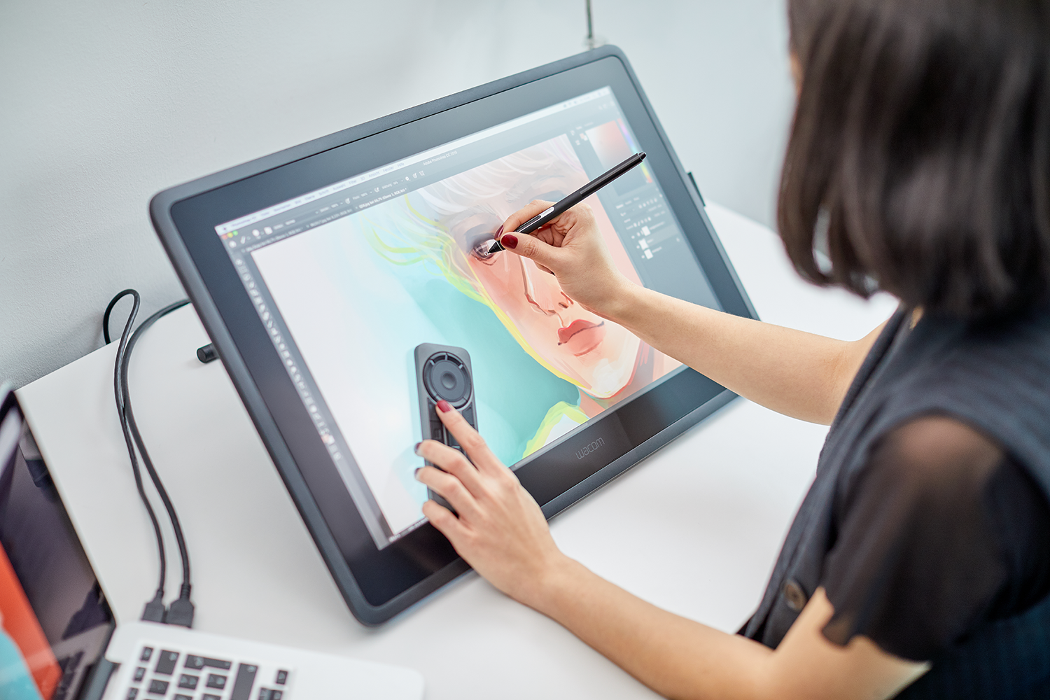 A woman drawing on a digital tablet with a stylus, a laptop is on the side.