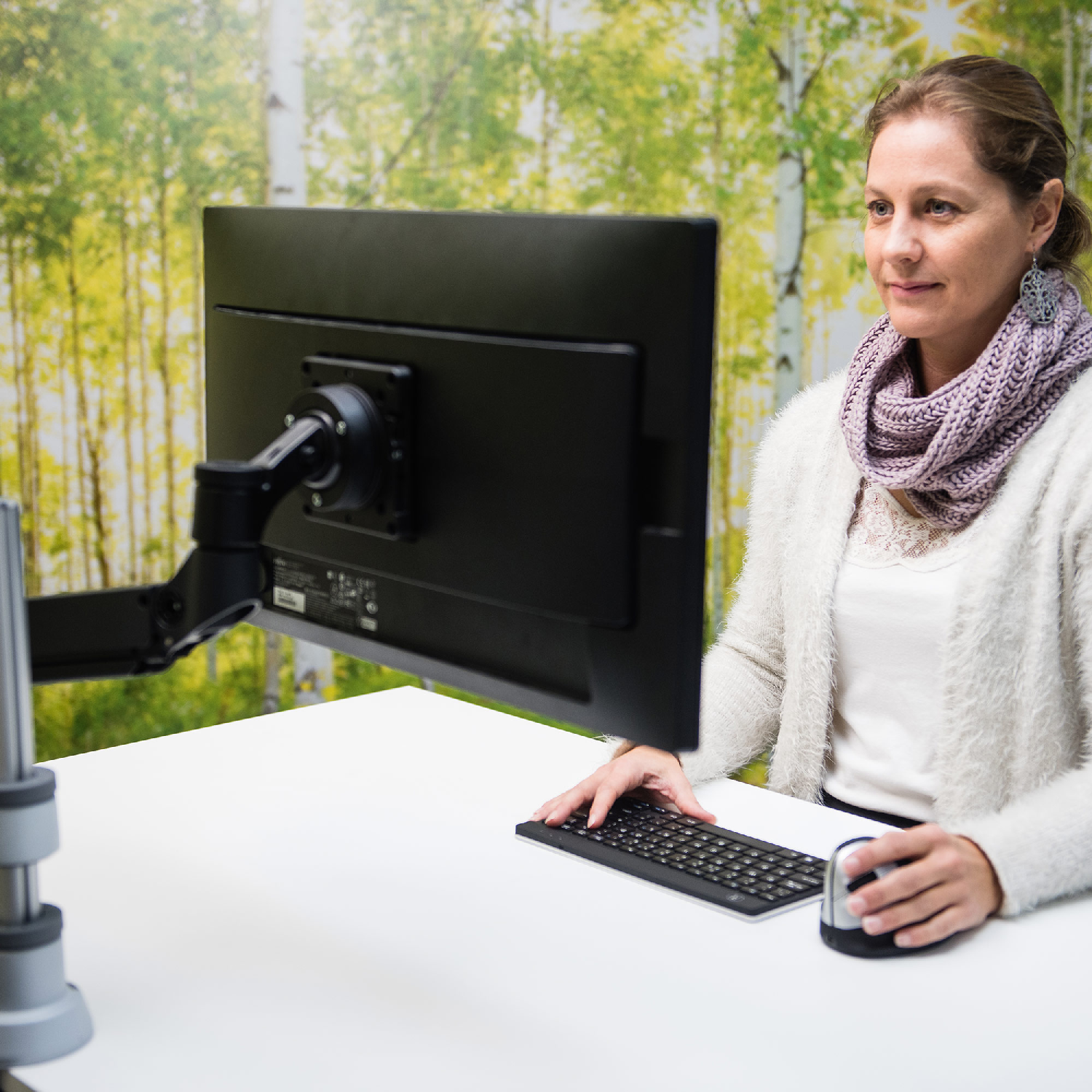 A woman is working at a white desk with a monitor, keyboard, and a mouse. Green background.