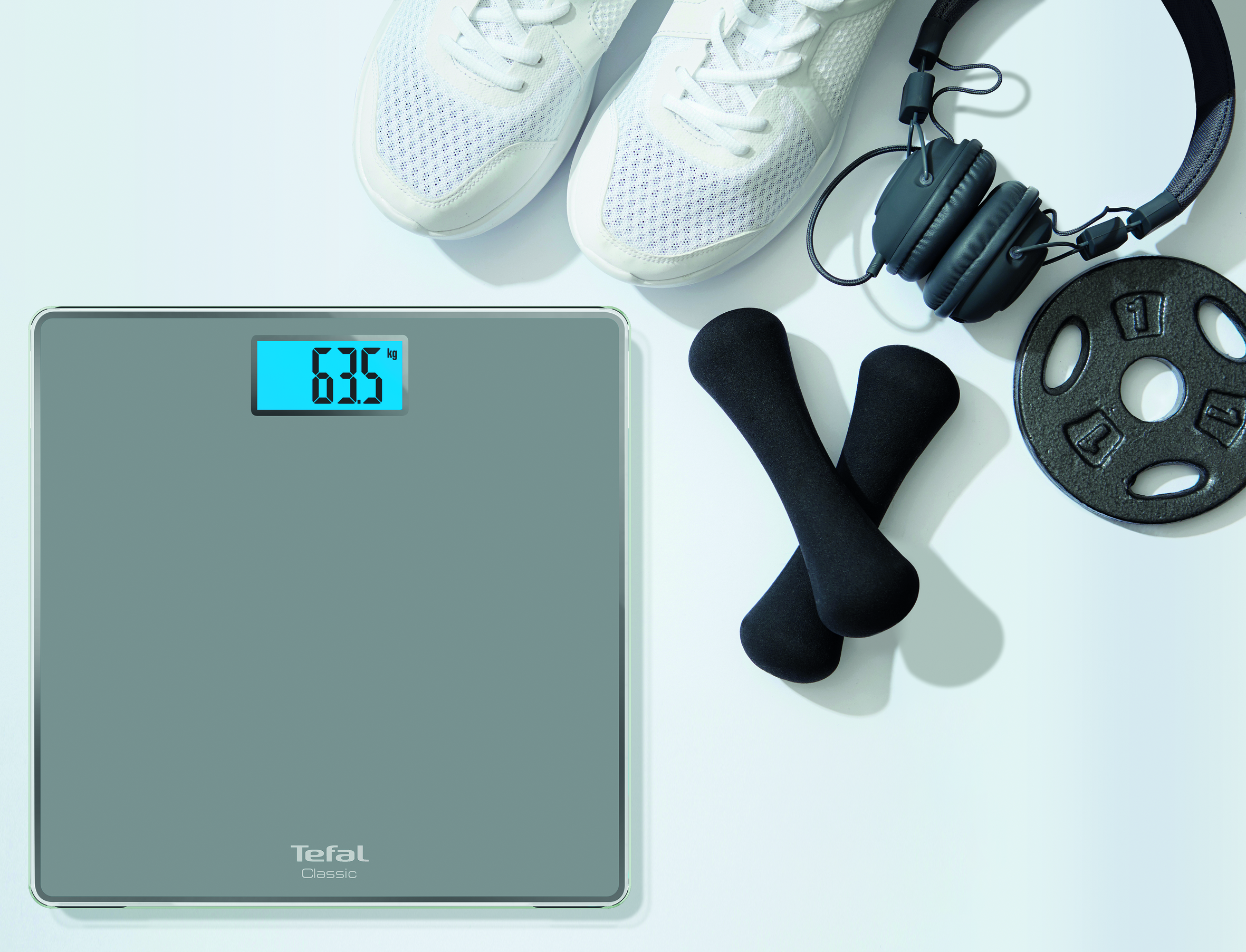 Een digitale weegschaal met 63,5 kg, met dumbbells en een koptelefoon.