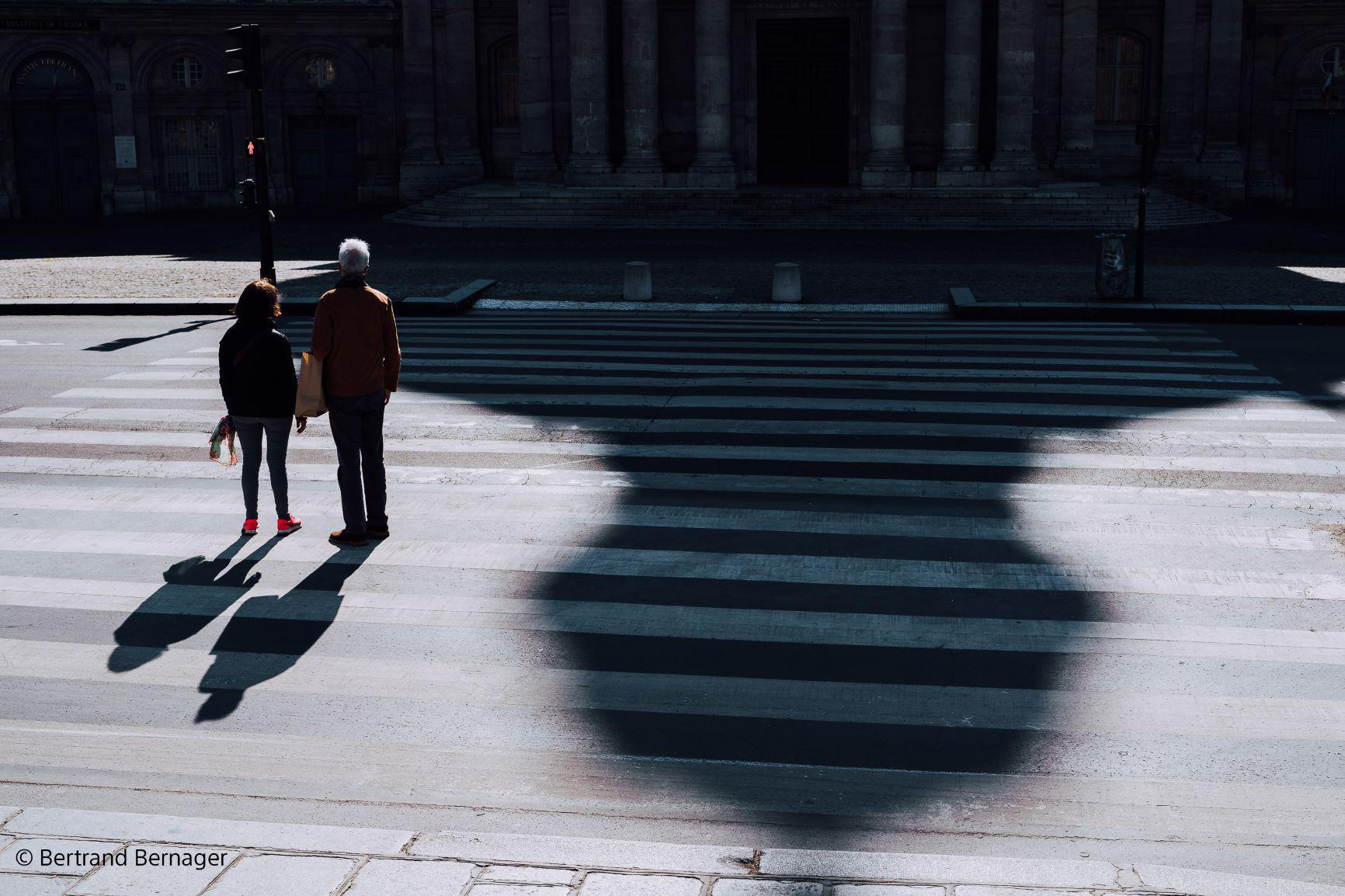 Personen überqueren einen Zebrastreifen. Schatten der Personen fallen auf den Zebrastreifen.
