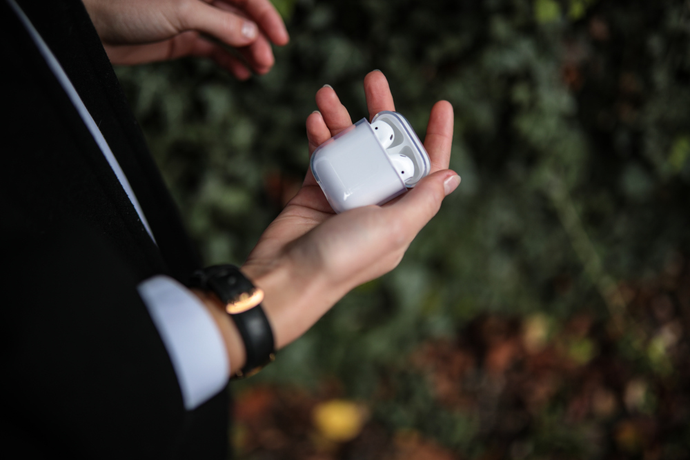 Person holding white AirPods case with AirPods inside, in a natural setting.