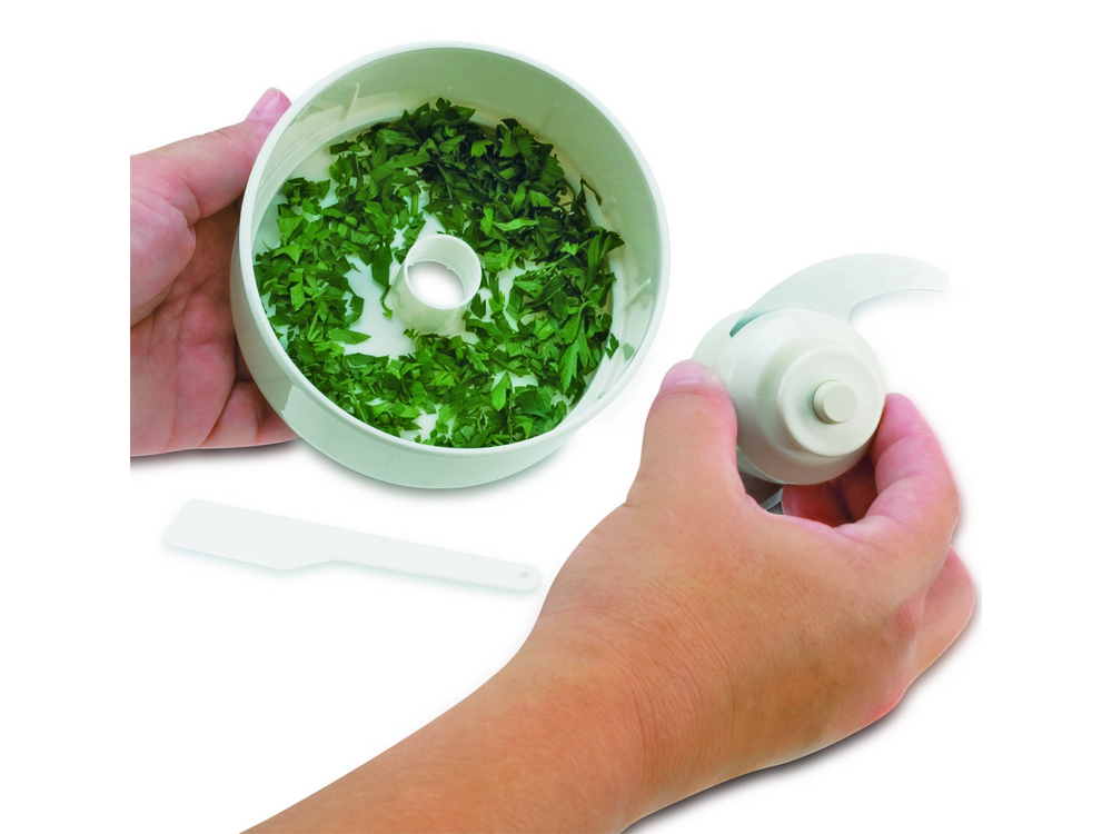 Manos montando un procesador de alimentos blanco con hierbas verdes.