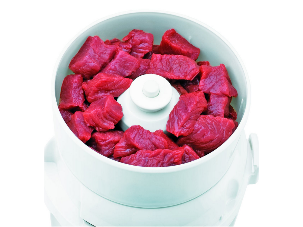 Un cuenco blanco de procesador de alimentos lleno de trozos de carne roja. El fondo es blanco.