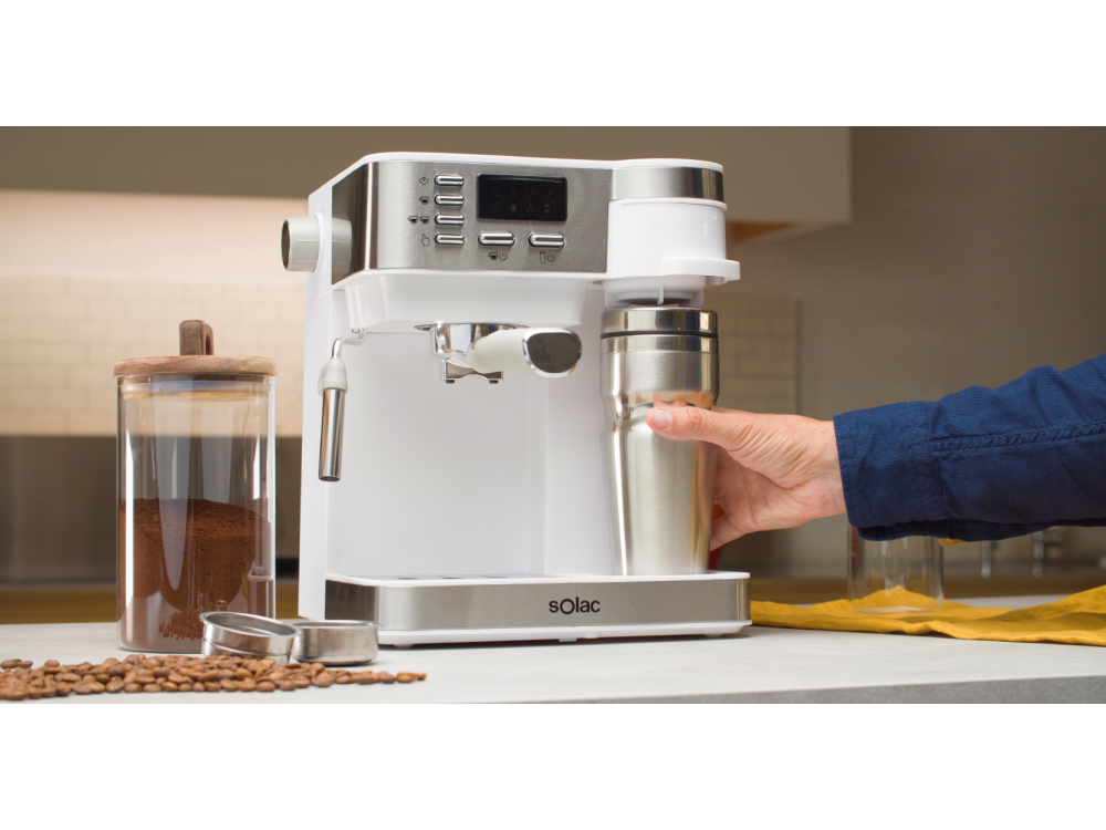 Una máquina de espresso blanca y plateada está sobre la encimera. Una taza plateada está lista.