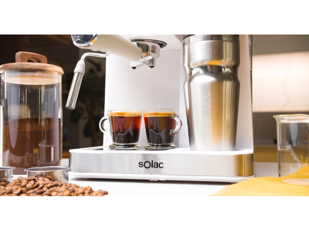 Una máquina de espresso con dos tazas de café, un termo de acero inoxidable y granos de café.
