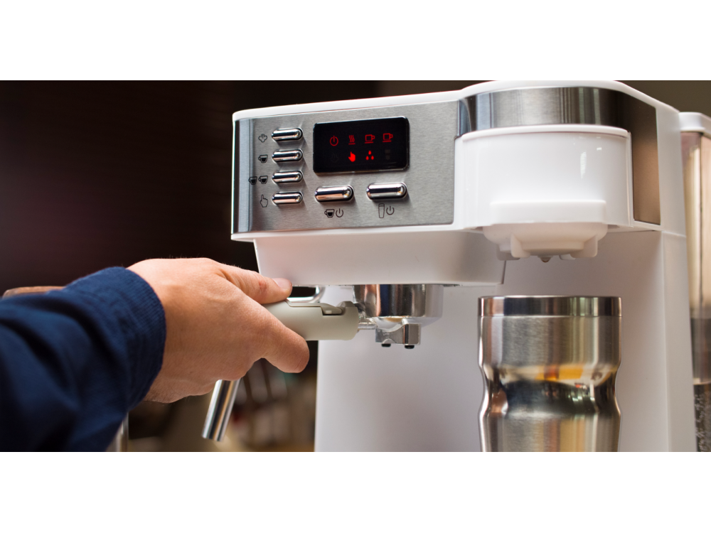 Una persona usando una máquina de espresso blanca, sosteniendo el mango, con una taza de metal.