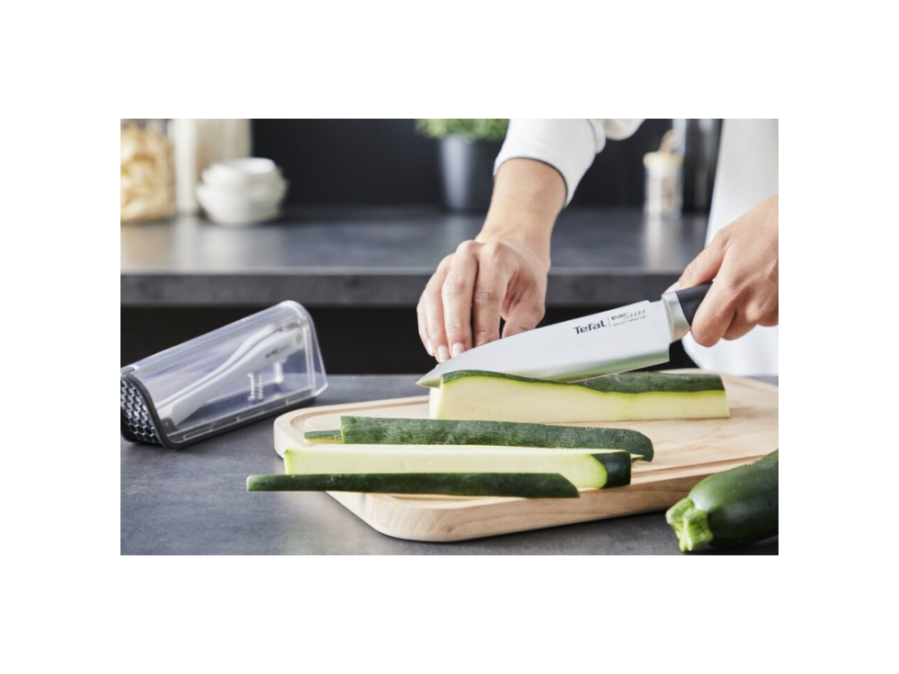 Persona cortando calabacín en una tabla de madera con un cuchillo, con más calabacín cerca.