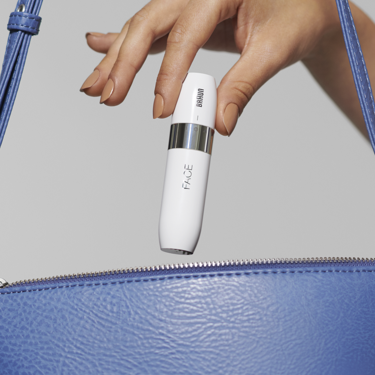 A hand holding a white beauty device over a blue purse.