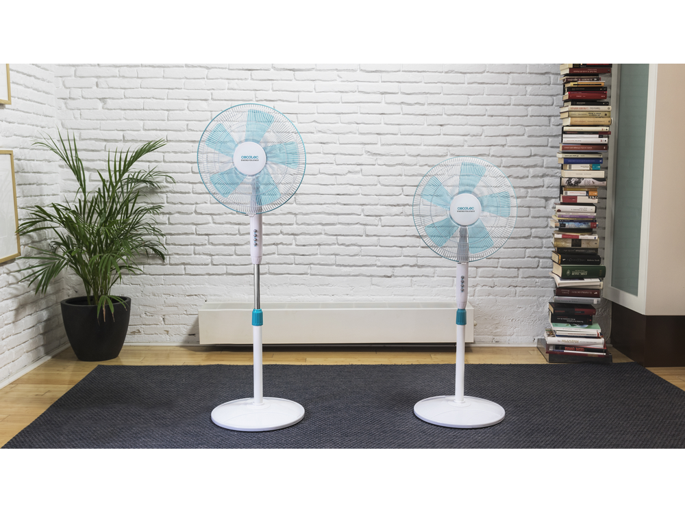 Dos ventiladores de pie blancos y turquesa sobre una alfombra gris oscura frente a una pared de ladrillos blancos.