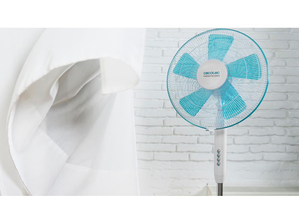 Ventilador blanco con aspas azules frente a pared de ladrillos blancos y tela blanca.