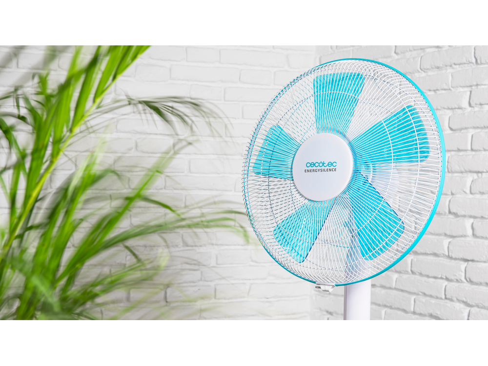 Un ventilador Cecotec EnergySilence blanco con aspas turquesas, frente a una pared de ladrillos blancos.