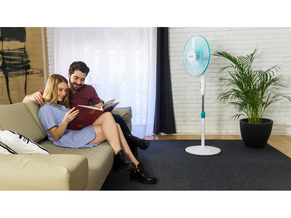 Una pareja sentada en un sofá leyendo un libro. Un ventilador a la derecha.