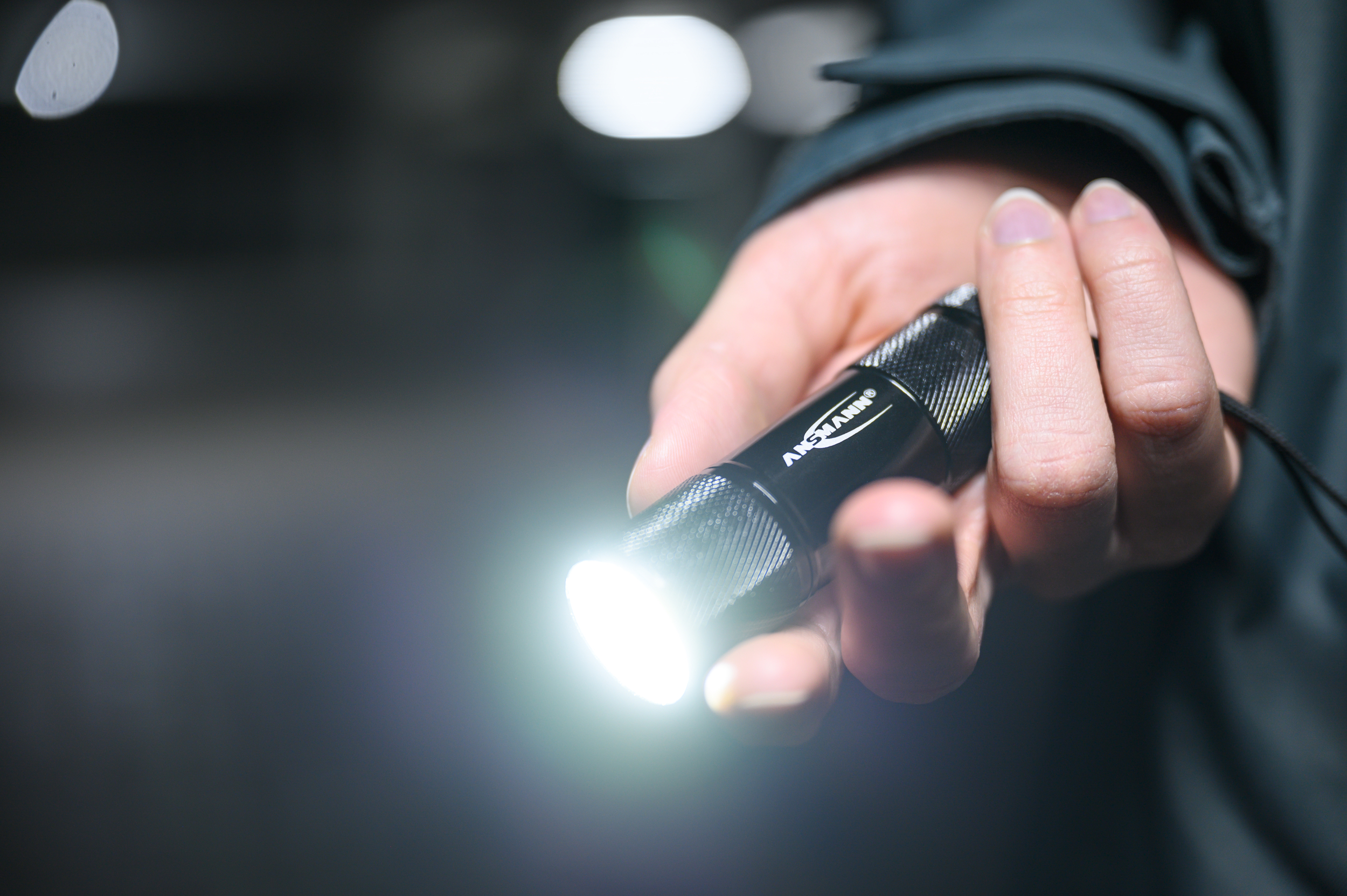 Hand, die eine schwarze Taschenlampe mit hellem Licht hält.