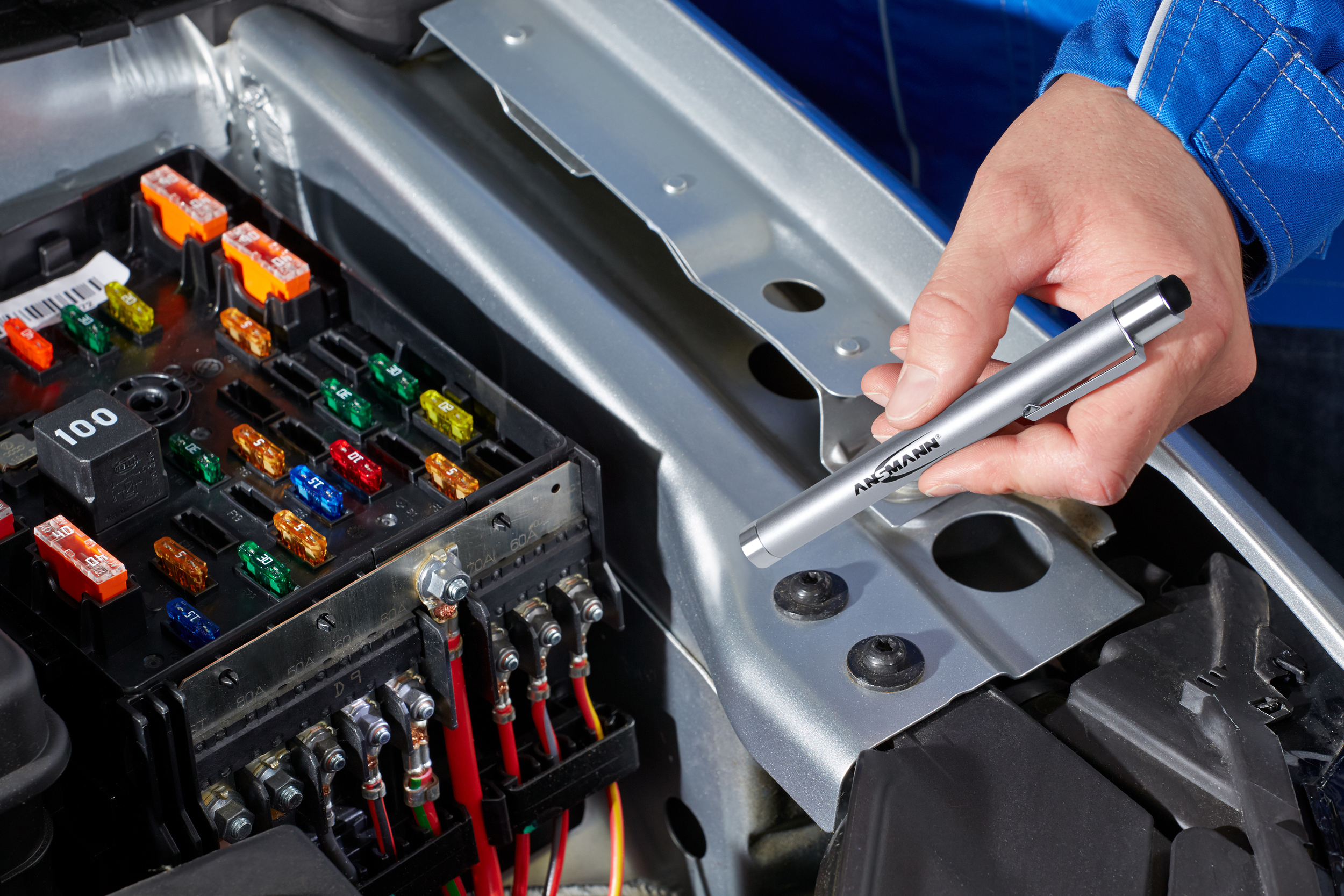 Die Hand einer Person hält einen Stift und untersucht Autosicherungen im Motorraum.