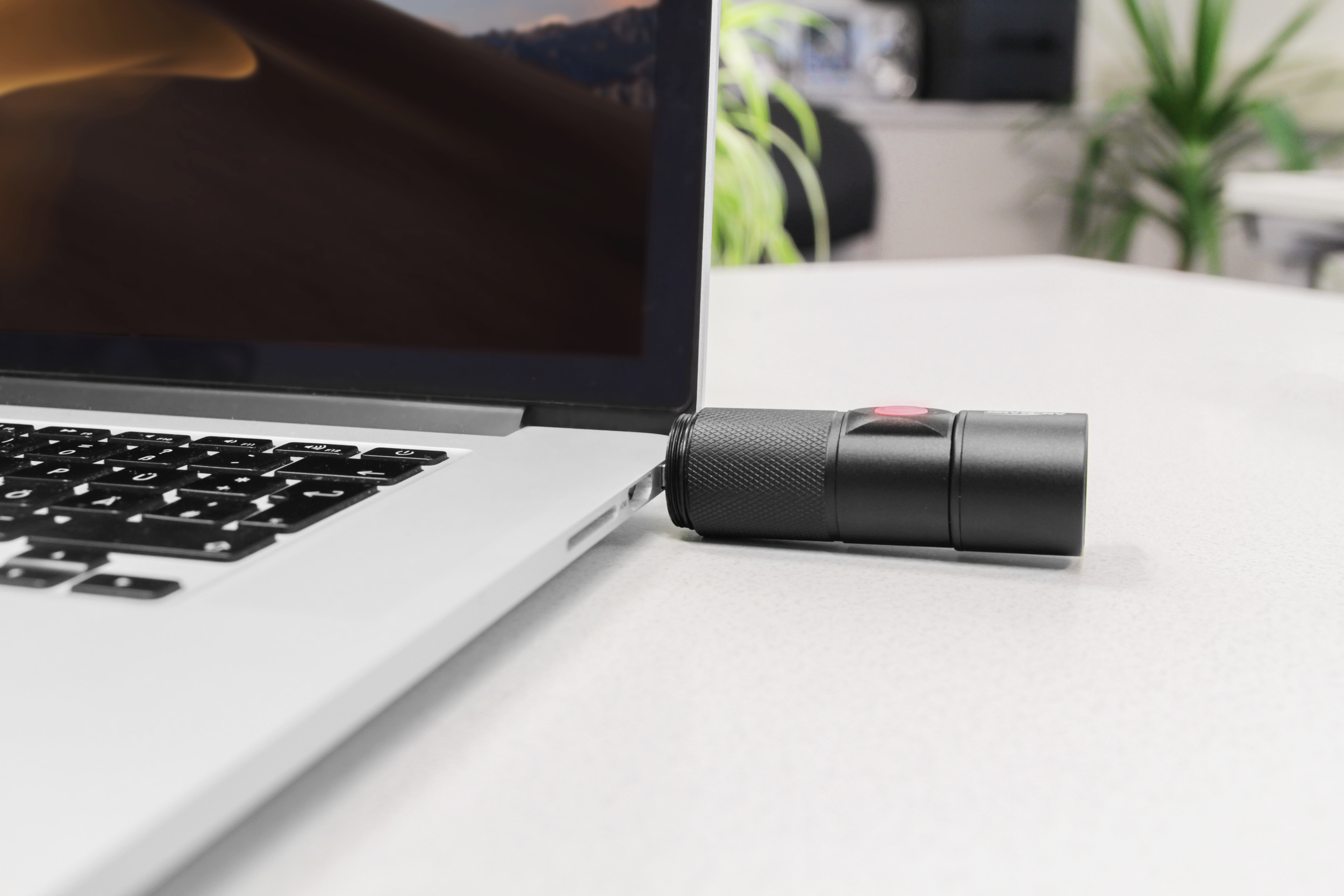 Ein Laptop mit einem schwarzen USB-Mikrofon, das angeschlossen ist und auf einer weißen Oberfläche liegt.