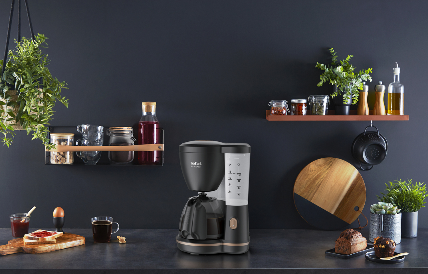 Keuken met koffiezetapparaat, eten en keukengerei op een donker oppervlak.