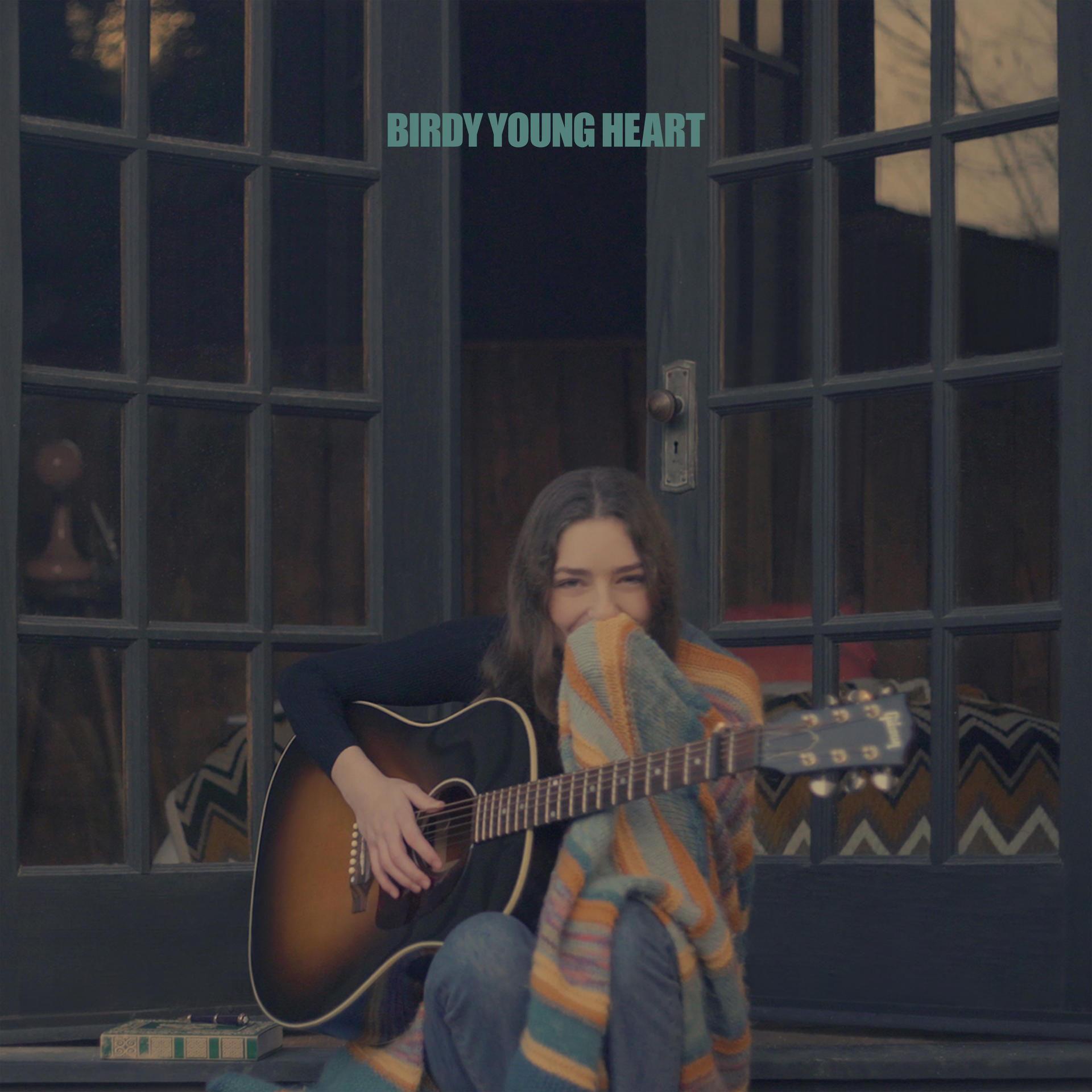 Album borító. Lány gitározik egy ajtó előtt. Cím: Birdy Young Heart.