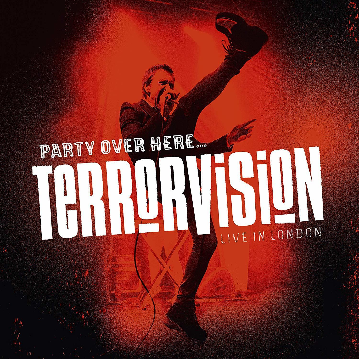 Egy öltönyös férfi vörös színpadon lép fel, a TERRORVISION szóval fehér színben. Felrúgott egy lábat.