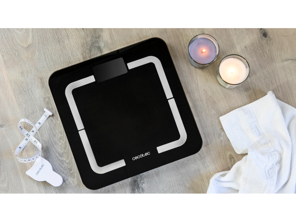 Báscula negra con borde blanco, velas y cinta métrica en suelo de madera.