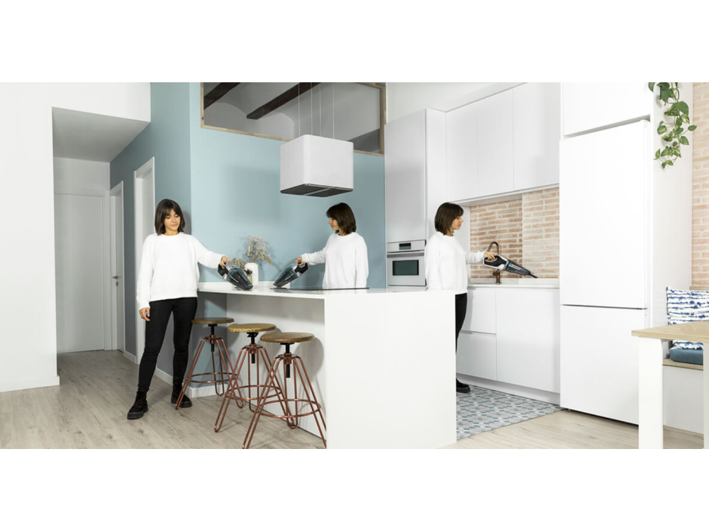 Mujer usando una aspiradora de mano en una cocina moderna.