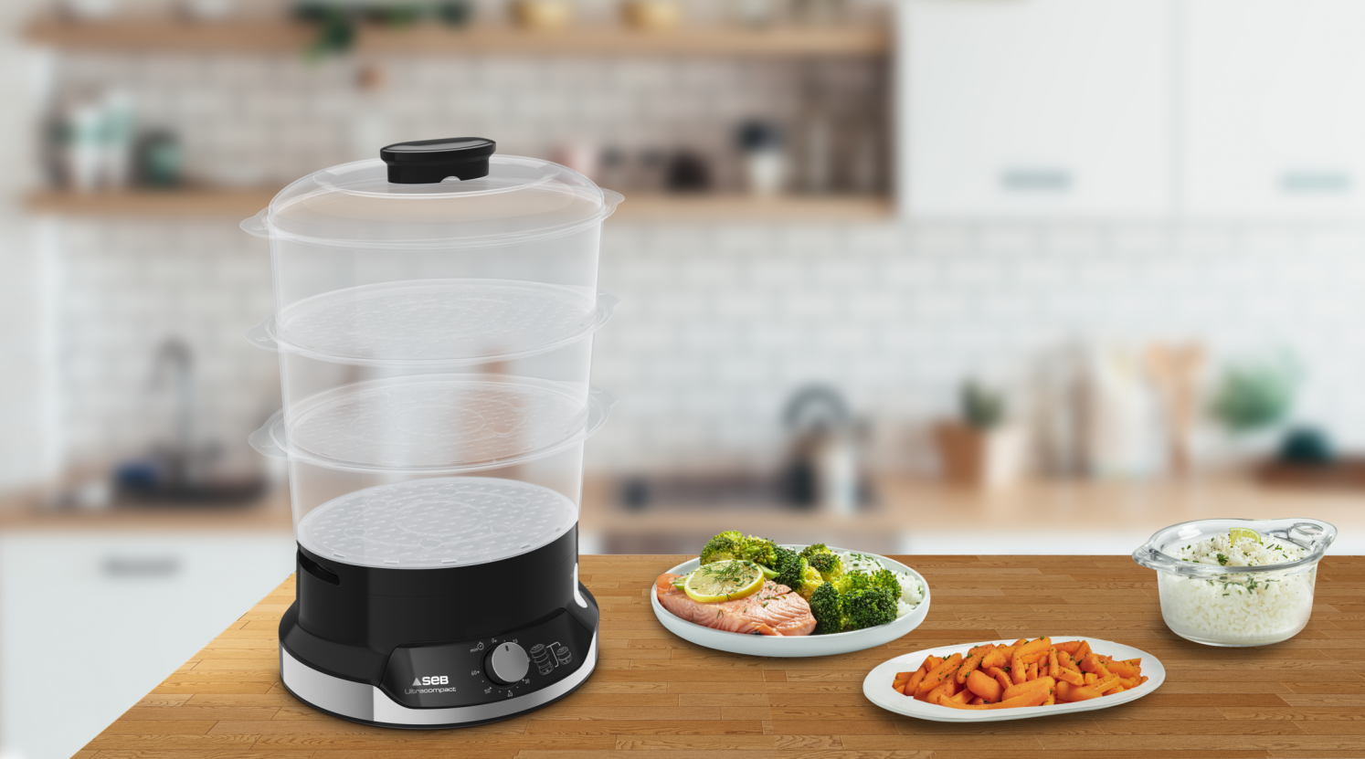 A three-tiered food steamer with food on plates, including broccoli, carrots, and rice, on a wooden table.