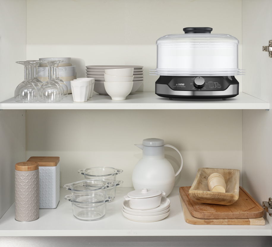 Kitchen cabinet with a steamer, glasses, plates, bowls, and jars.