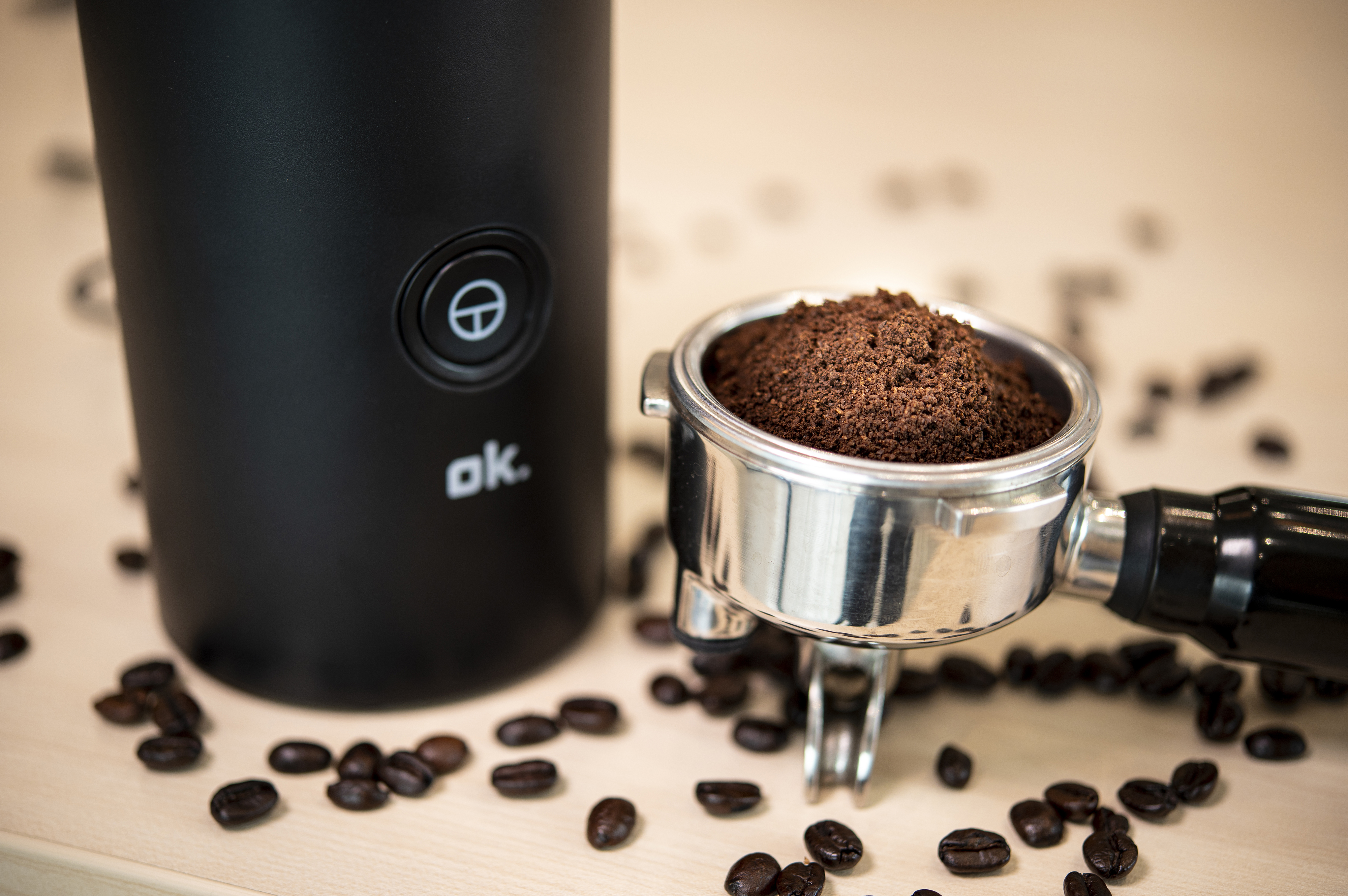 Coffee grinder with ground coffee in a portafilter. Coffee beans are scattered around.